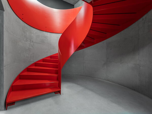 Rote Metall-Wendeltreppe aus Stahl in grauem Betonraum